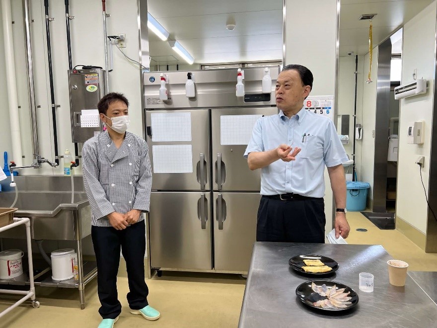 佐藤日呂登代表取締役社長から魚の燻製について説明を受け、試食をする知事
