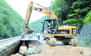 豪雨で陥没した道路の復旧作業を行う建設作業員の写真