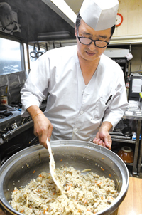 炊き上がったばかりの舞茸ごはんを混ぜる柏富芳さんの写真