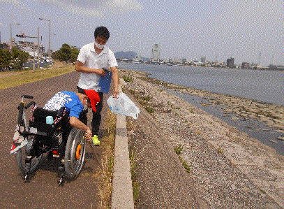 車椅子に乗り湖岸土手の草取りをする様子