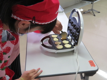 混ぜた材料を焼きドーナツメーカーに入れる児童