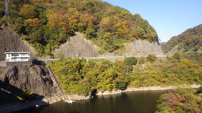 ダム管理所背景の紅葉とみやび湖面の写真です。