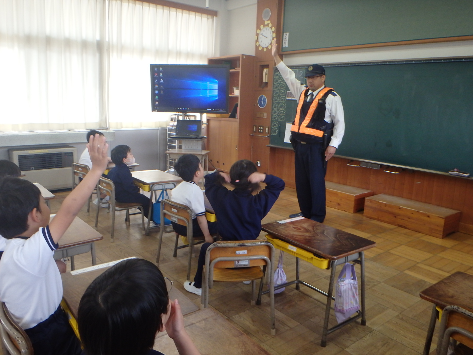 津和野警察署の警察官が小学生に手を上げる方法を教えています。