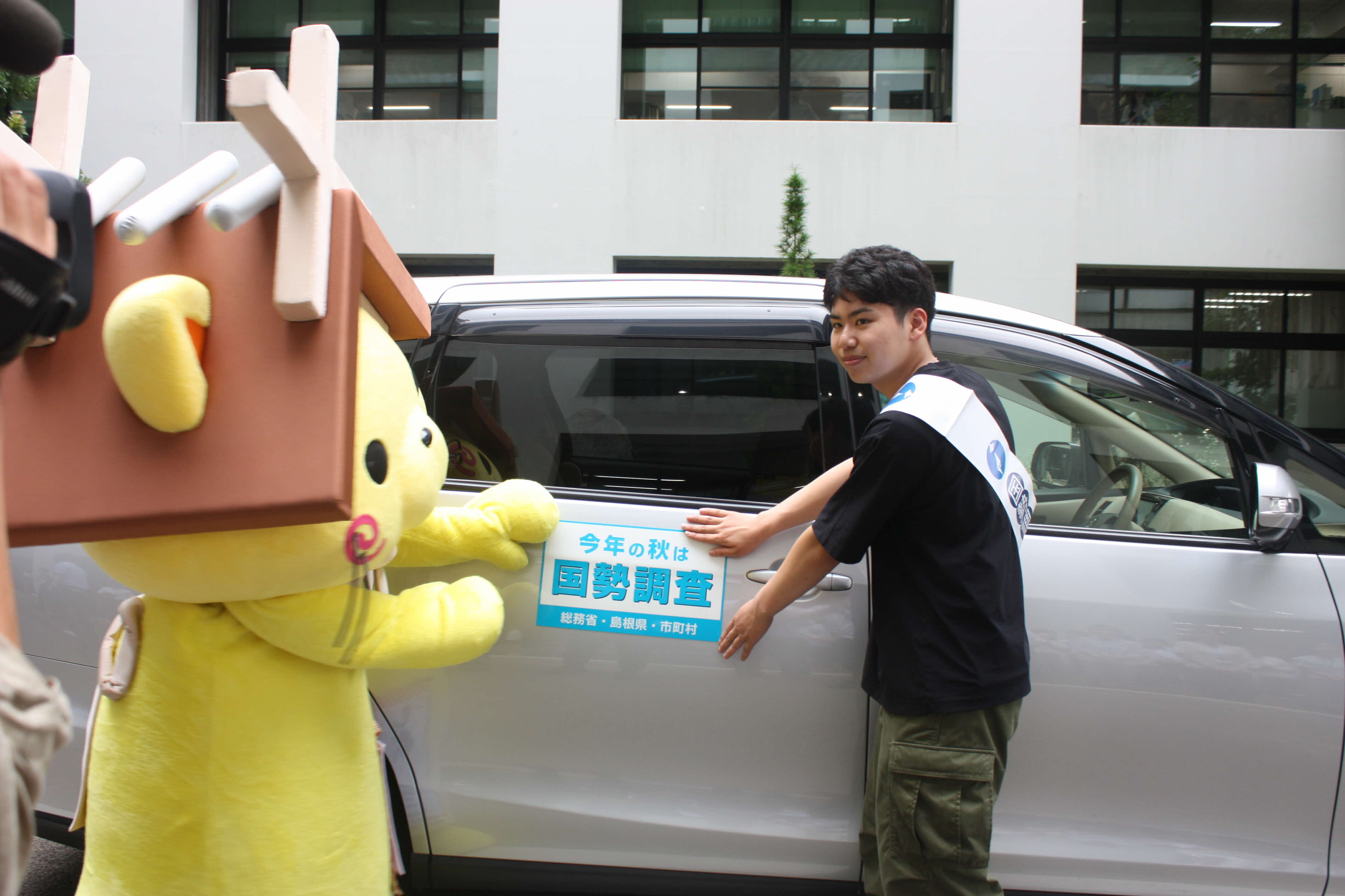 マグネットシートを貼る学生調査員と島根県観光キャラクターしまねっこ